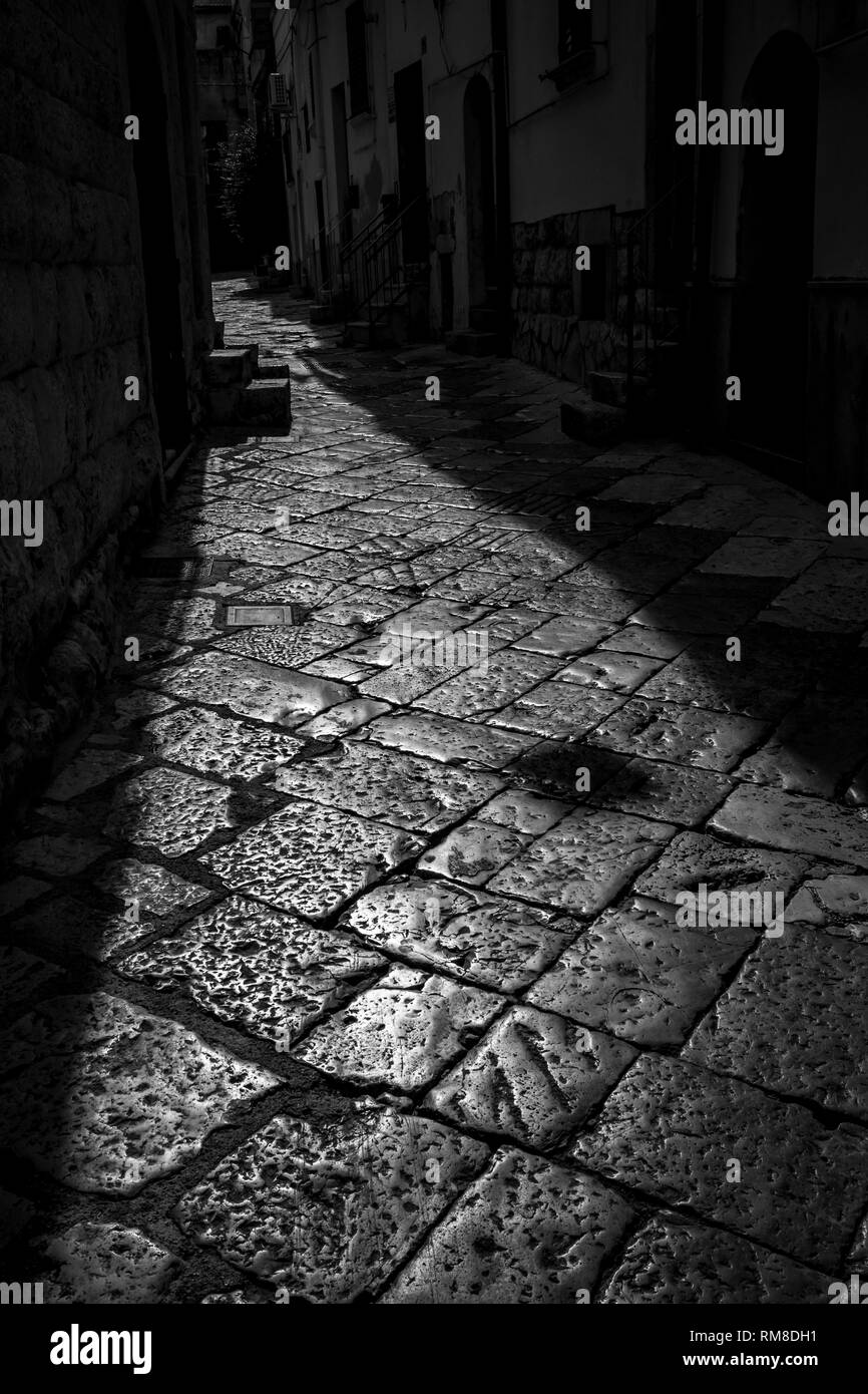 Schöne Sonne beleuchteten Stein Gasse in Altamura, Apulien, Italien. Schwarze und weiße hoher Kontrast Foto gegen die Sonne Licht im sonnigen Sommer Nachmittag im alten Zentrum der herrlichen Stadt Stockfoto