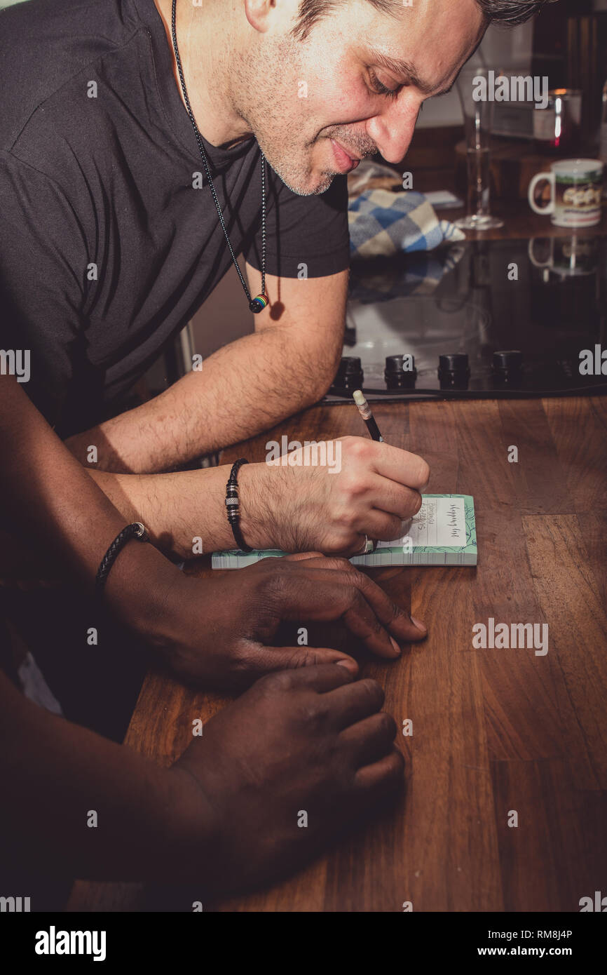 Ein interracial Gay Paare bilden eine Einkaufsliste für Lebensmittel auf einer hölzernen küche top zu Hause. Stockfoto