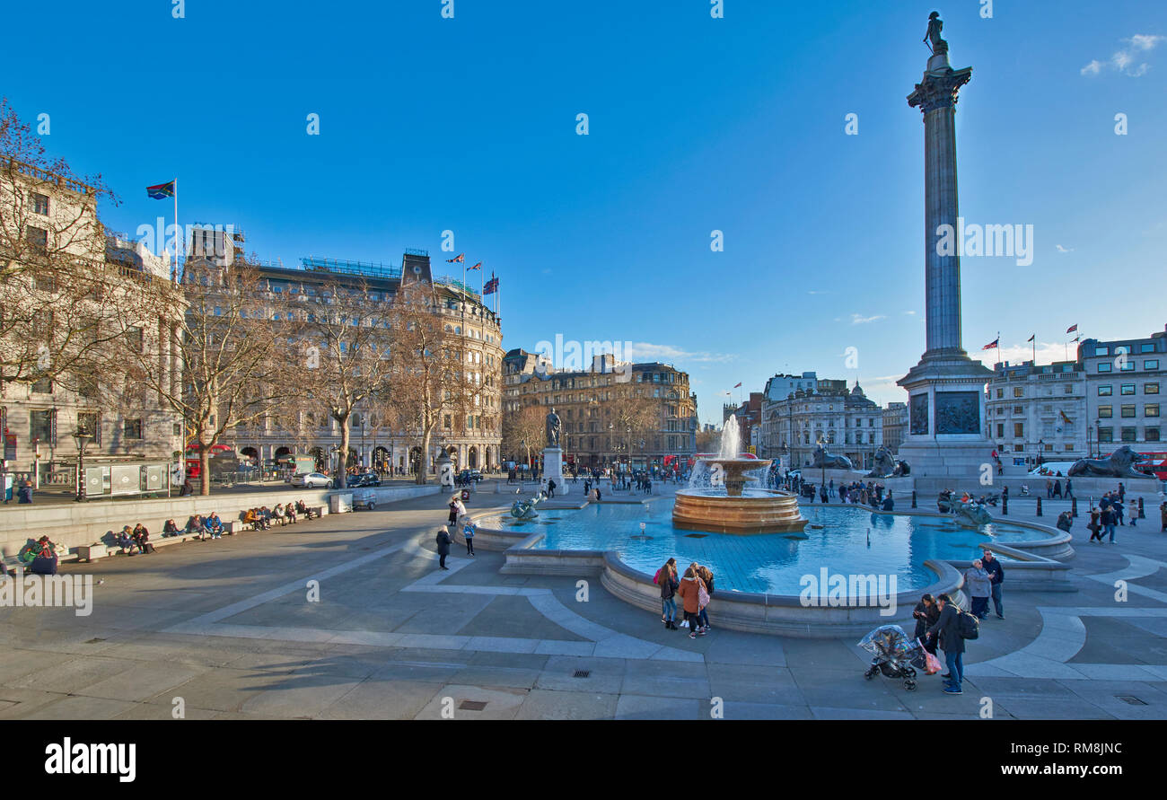 LONDON Trafalgar Square Brunnen und NELSONS COLUMN MIT MENSCHEN SITZEN IM WINTER SONNENSCHEIN Stockfoto