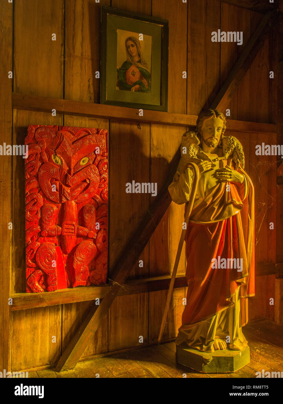 Maori Schnitzereien und die Statue von Christus, dem Guten Hirten, mellow goldenes Licht auf Holz verkleideten Wänden, Kirche, Pepara Koriniti Marae, Whanganui Stockfoto