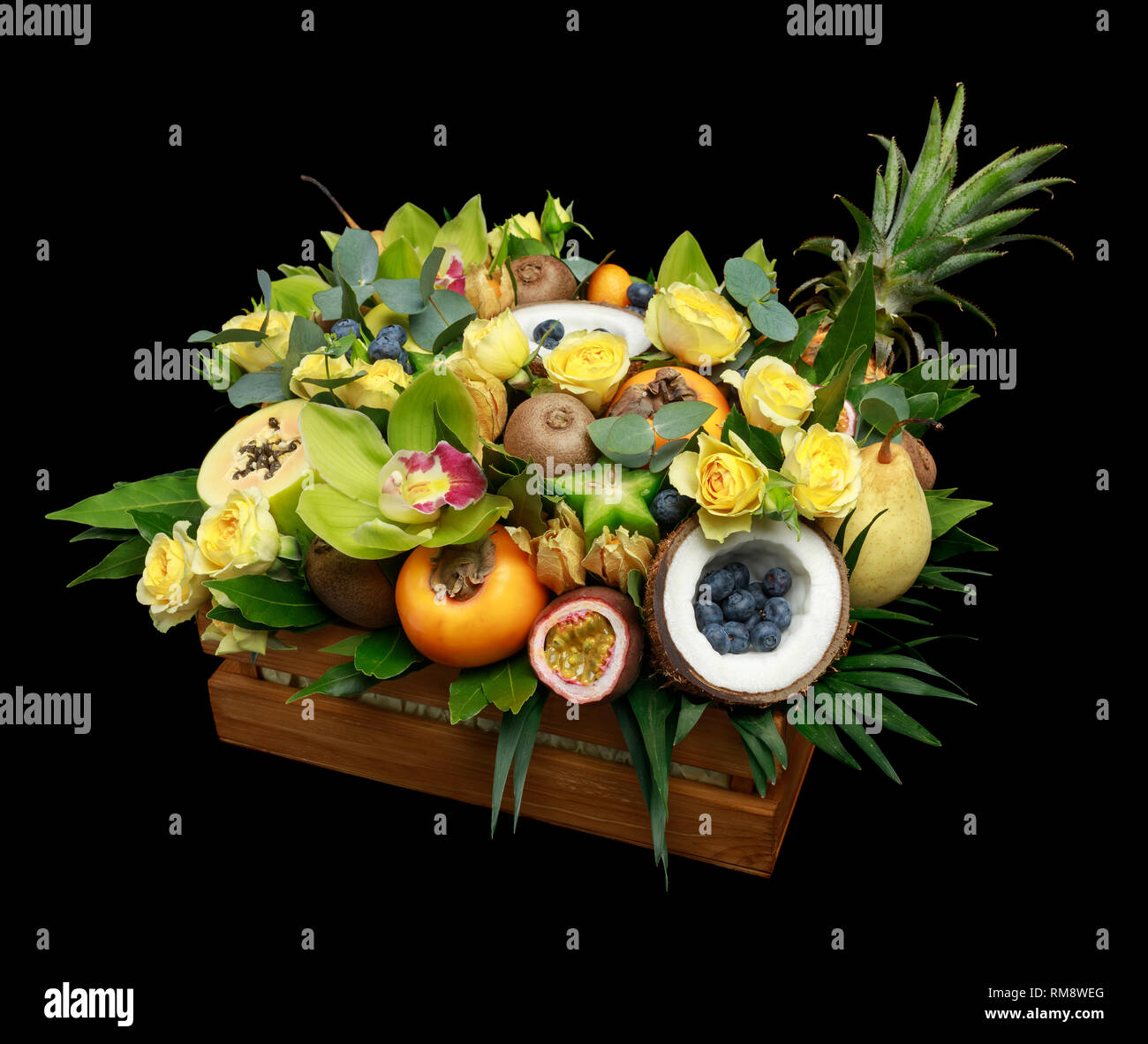 Holzkiste mit vielen exotischen Früchten und Blumen auf schwarzem Hintergrund Stockfoto