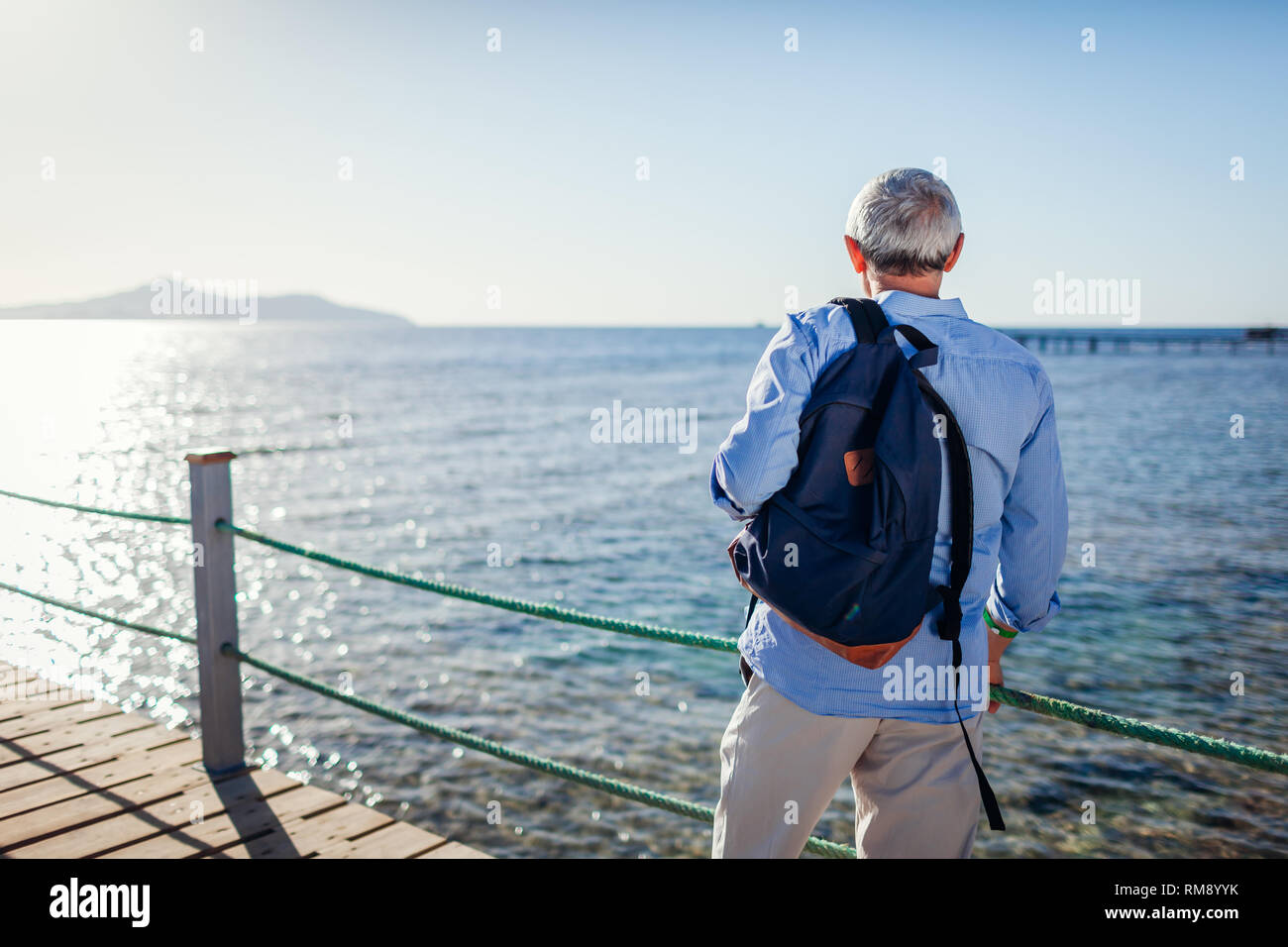 Älterer Mann mit Rucksack Landschaft bewundern, das Rote Meer und die Insel Tiran am Pier. Reisen und Tourismus Konzept. Sommer Urlaub Stockfoto Älterer Mann mit Rucksack Landschaft bewundern, das Rote Meer und die Insel Tiran am Pier. Reisen und Tourismus Konzept. Sommer Urlaub Stockfoto
