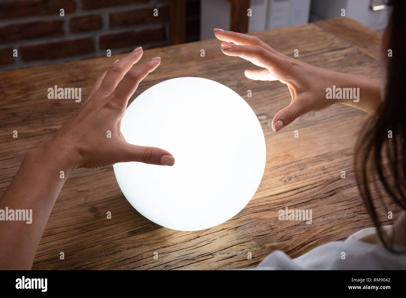 Nahaufnahme der Wahrsager Hand, die den glühenden Crystal Ball auf Schreibtisch Stockfoto