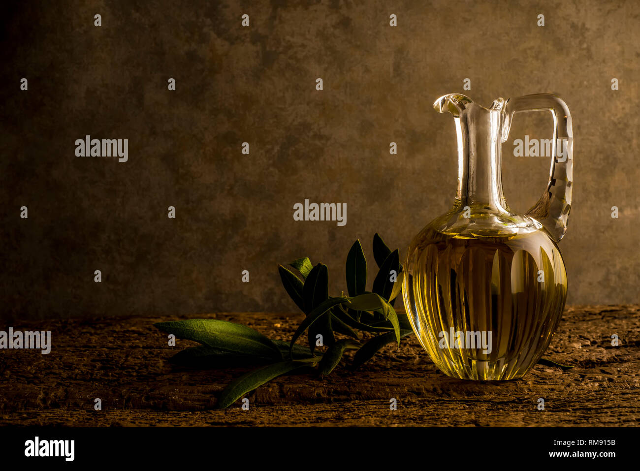 Natives Olivenöl in vintage Glas Öl jar und einen Olivenzweig in einer ockerfarbenen Hintergrund mit leeren Raum für Nachricht Stockfoto