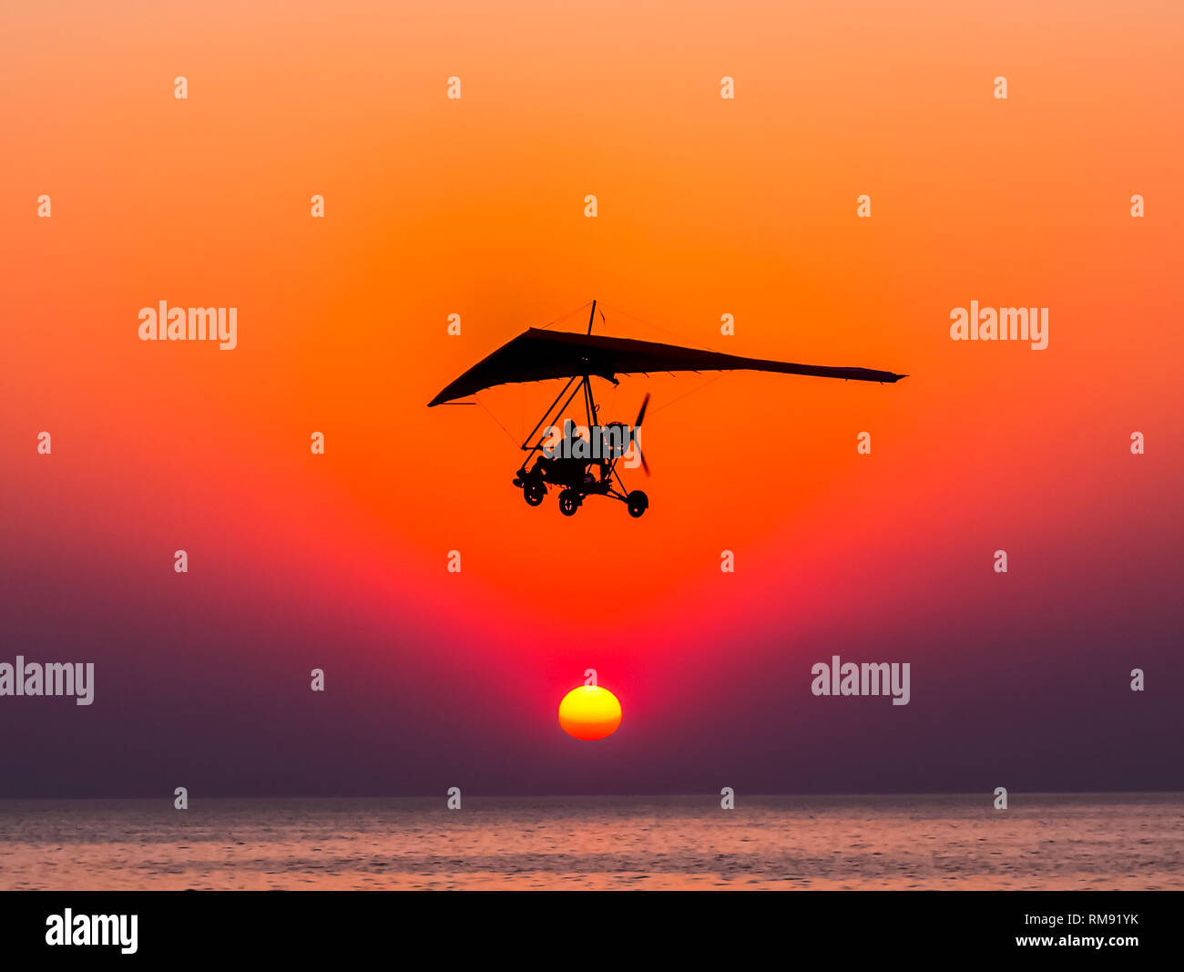 Die Person, die das Fliegen auf ein Trike mit den Motor gegen den Hängegleiter fliegt gegen den Sonnenuntergang. Stockfoto