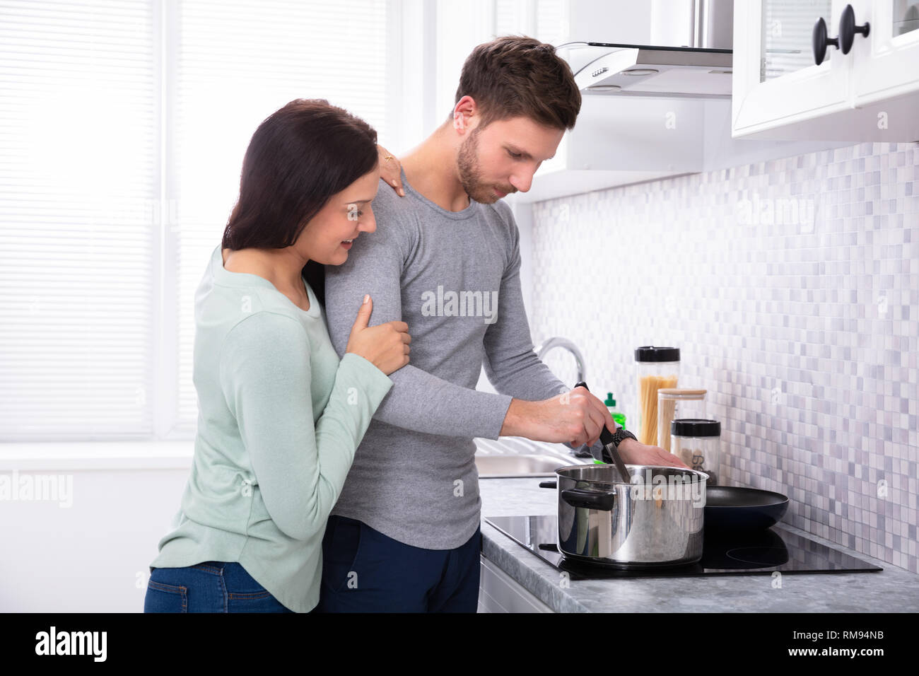 Junge Mann macht Essen mit seinem lächelnden Frau steht in der Küche Stockfoto