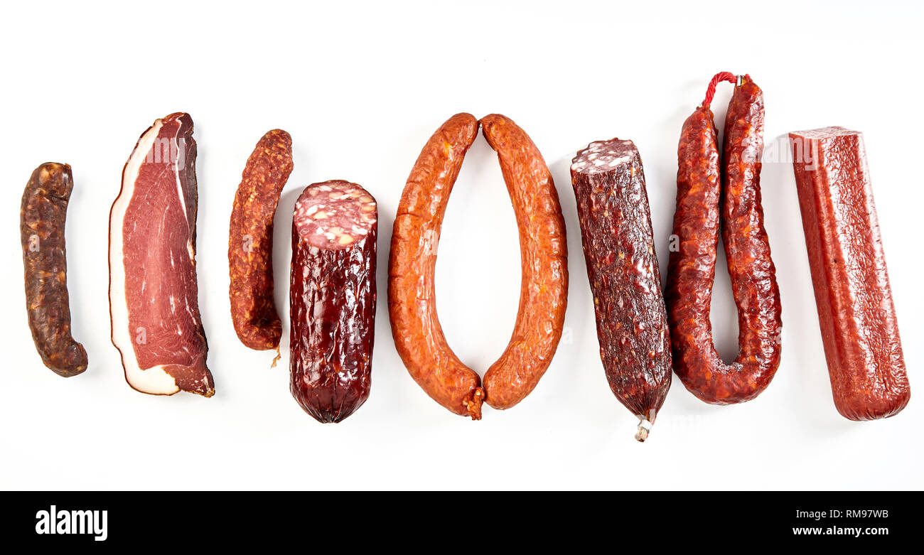 Köstliche Auswahl von würzigen getrockneten Würstchen mit einer Portion Schinken oder kassler arrangiert als flache noch Leben in einer Zeile isoliert auf weißem in einem Laien panor Stockfoto