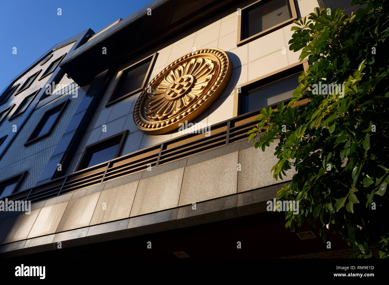 Goldenes Emblem auf dem modernen japanischen Gebäude mit Baum im Vordergrund bei Sonnenuntergang Stockfoto