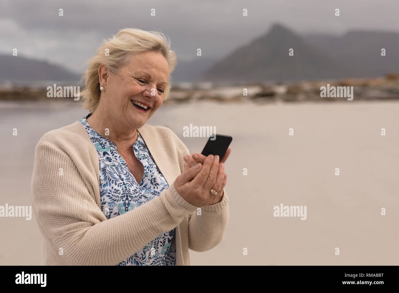 Gerne ältere Frau mit Handy am Strand Stockfoto