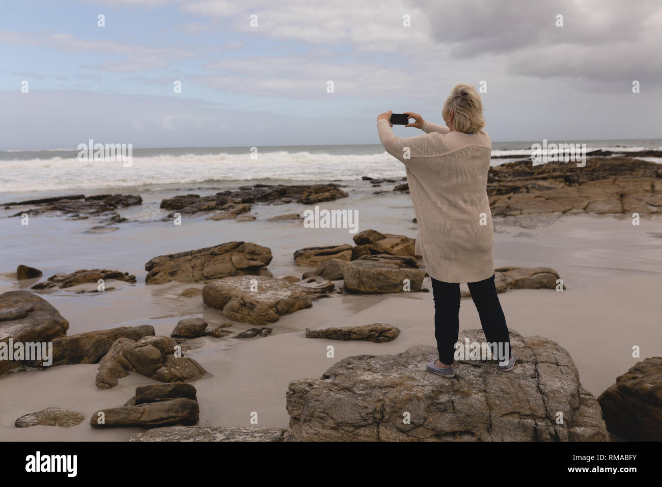Ältere Frau auf Fotos mit dem Handy am Strand Stockfoto