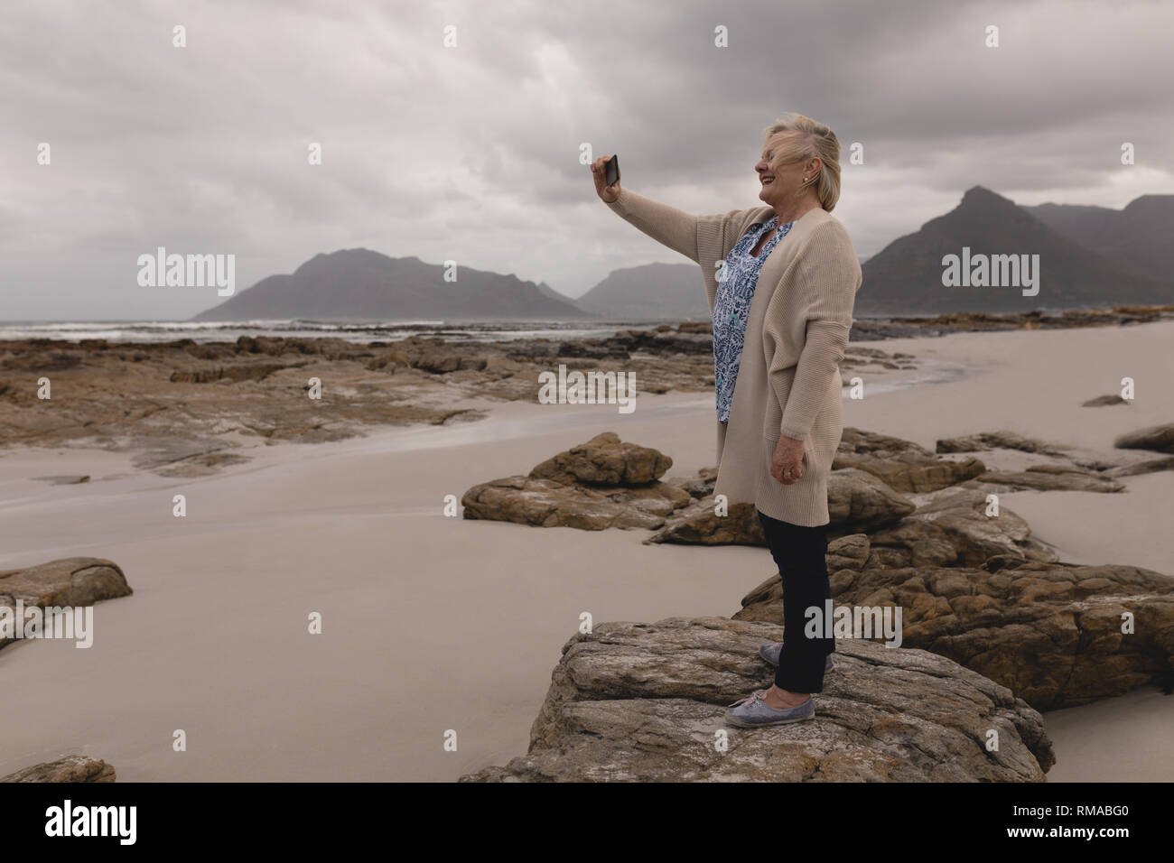 Ältere Frau auf Fotos mit dem Handy am Strand Stockfoto