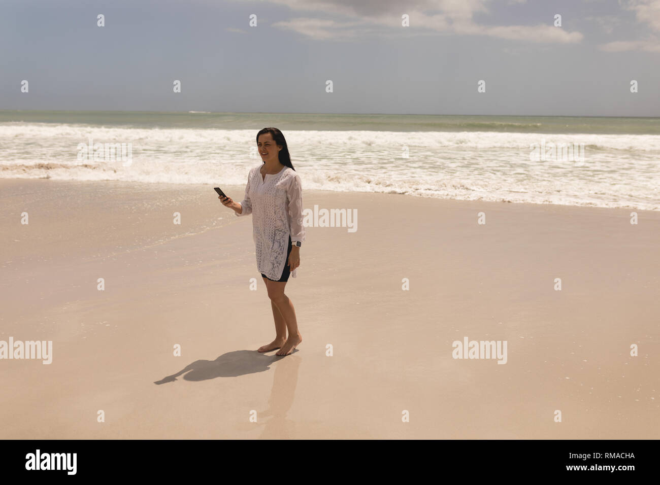 Junge Frau mit Handy am Strand Stockfoto