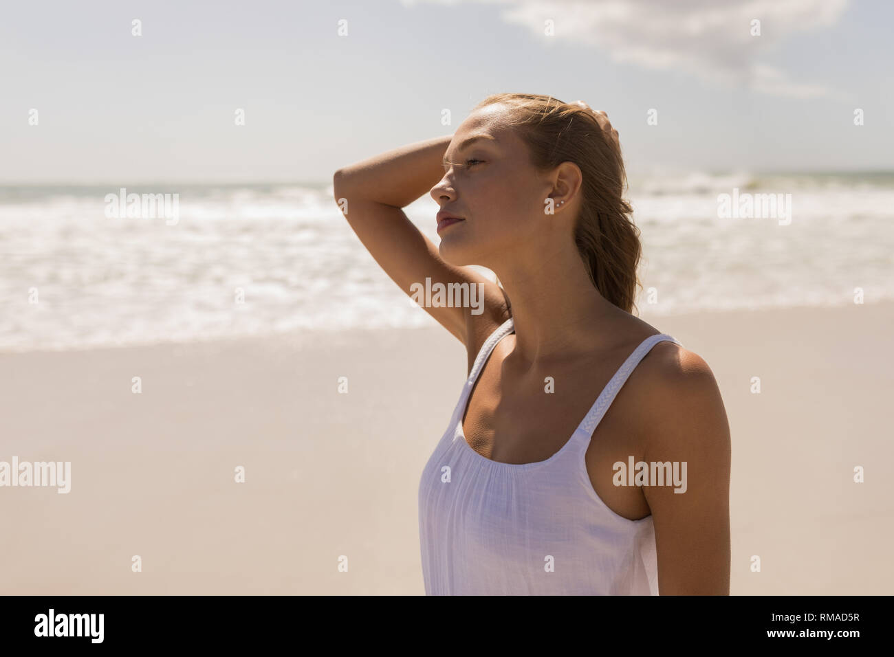Junge Frau mit der Hand auf den Kopf am Strand Stockfoto