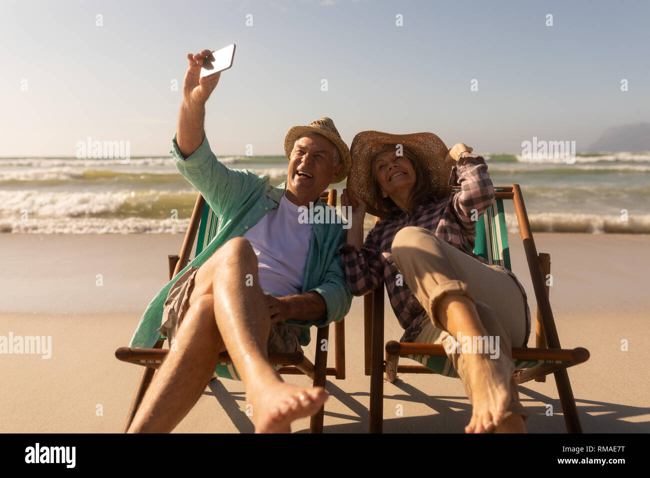 Senior Paar unter selfie mit Mobiltelefon, während Sie sich auf der Sonnenliege am Strand Stockfoto