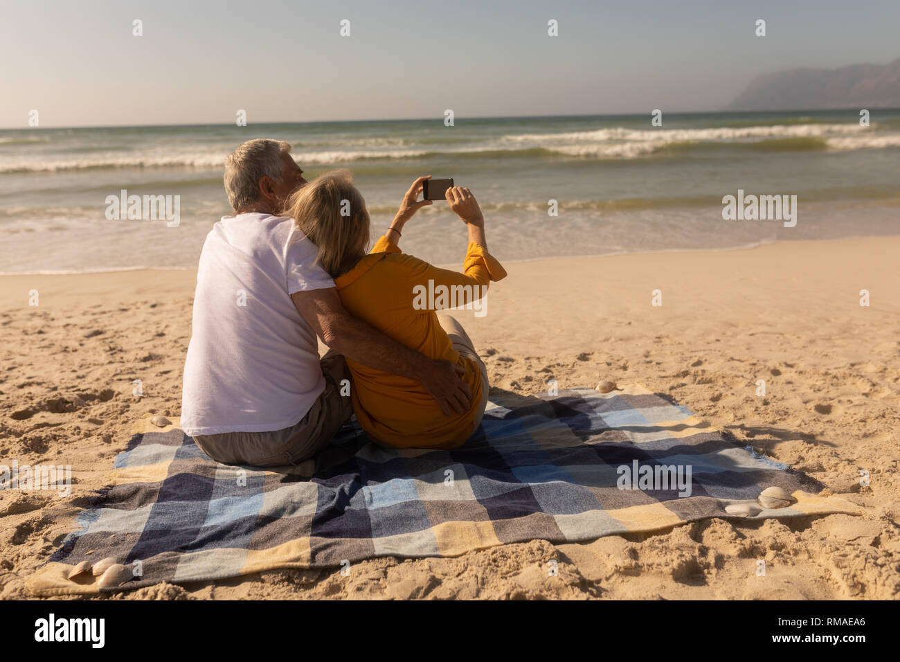 Senior Paar unter selfie mit Handy entspannen auf picknickdecke am Strand Stockfoto