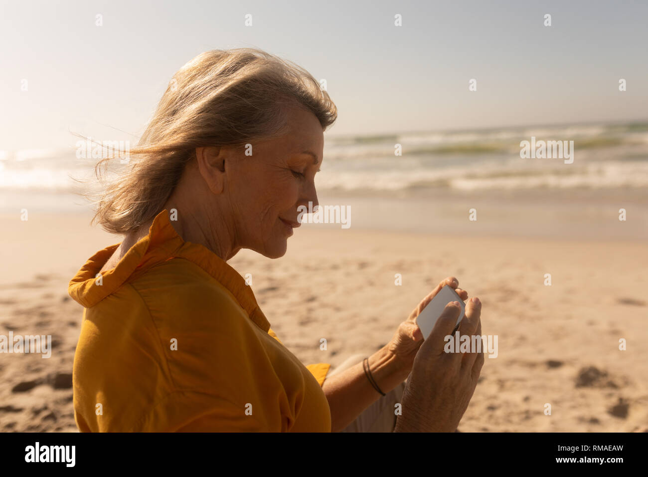 Ältere Frau Überprüfung durch Fotos auf Handy am Strand Stockfoto