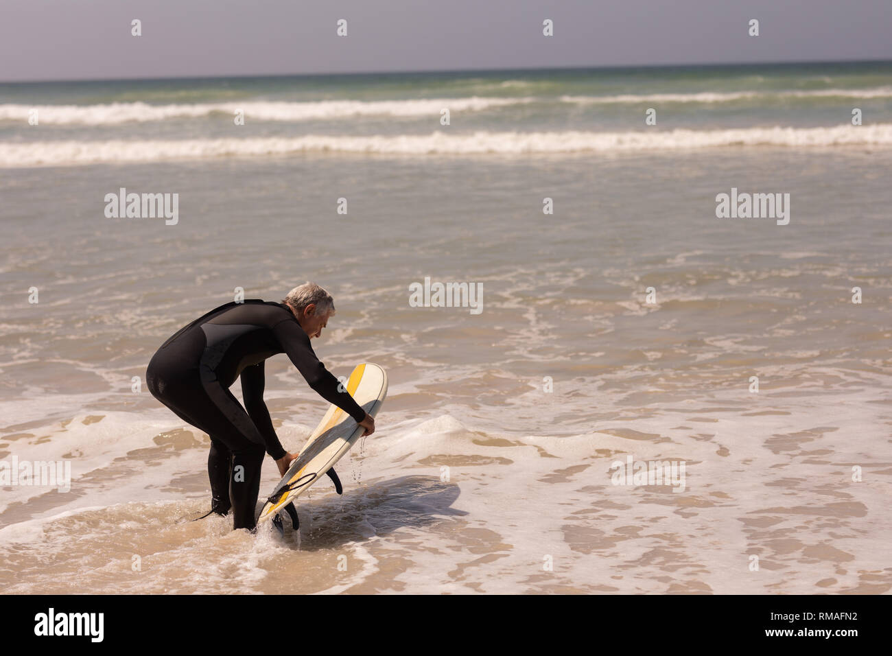 Ältere männliche Surfer mit Surfbrett surfen im Meer Stockfoto