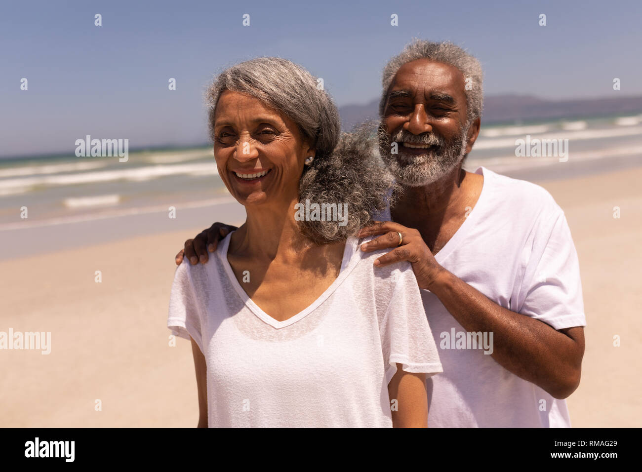 Älterer Mann stand mit den Händen auf ältere Frau Schultern am Strand Stockfoto