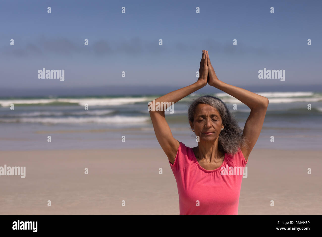 Ältere Frau mit geschlossenen Augen und gefalteten Händen Yoga am Strand. Stockfoto