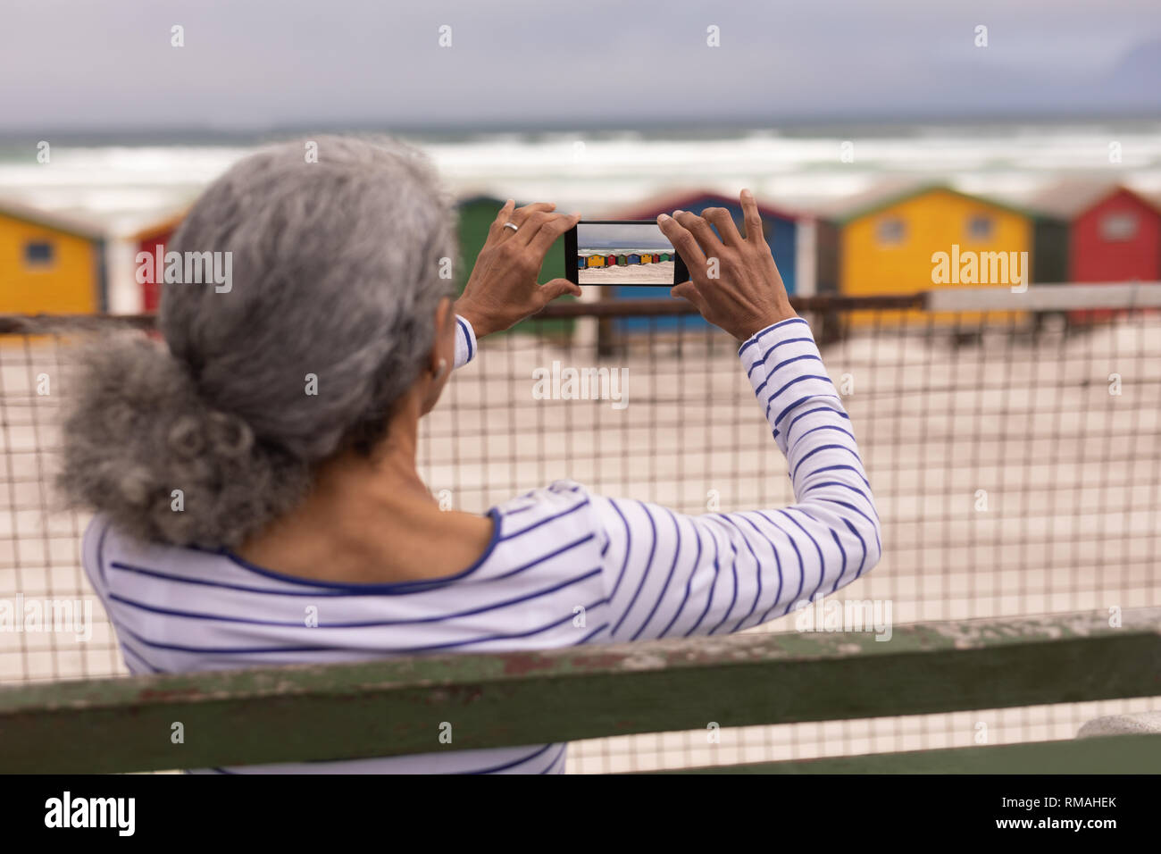 Ältere Frau Klick auf Foto mit Handy beim Sitzen auf der Promenade Sitzbank Stockfoto