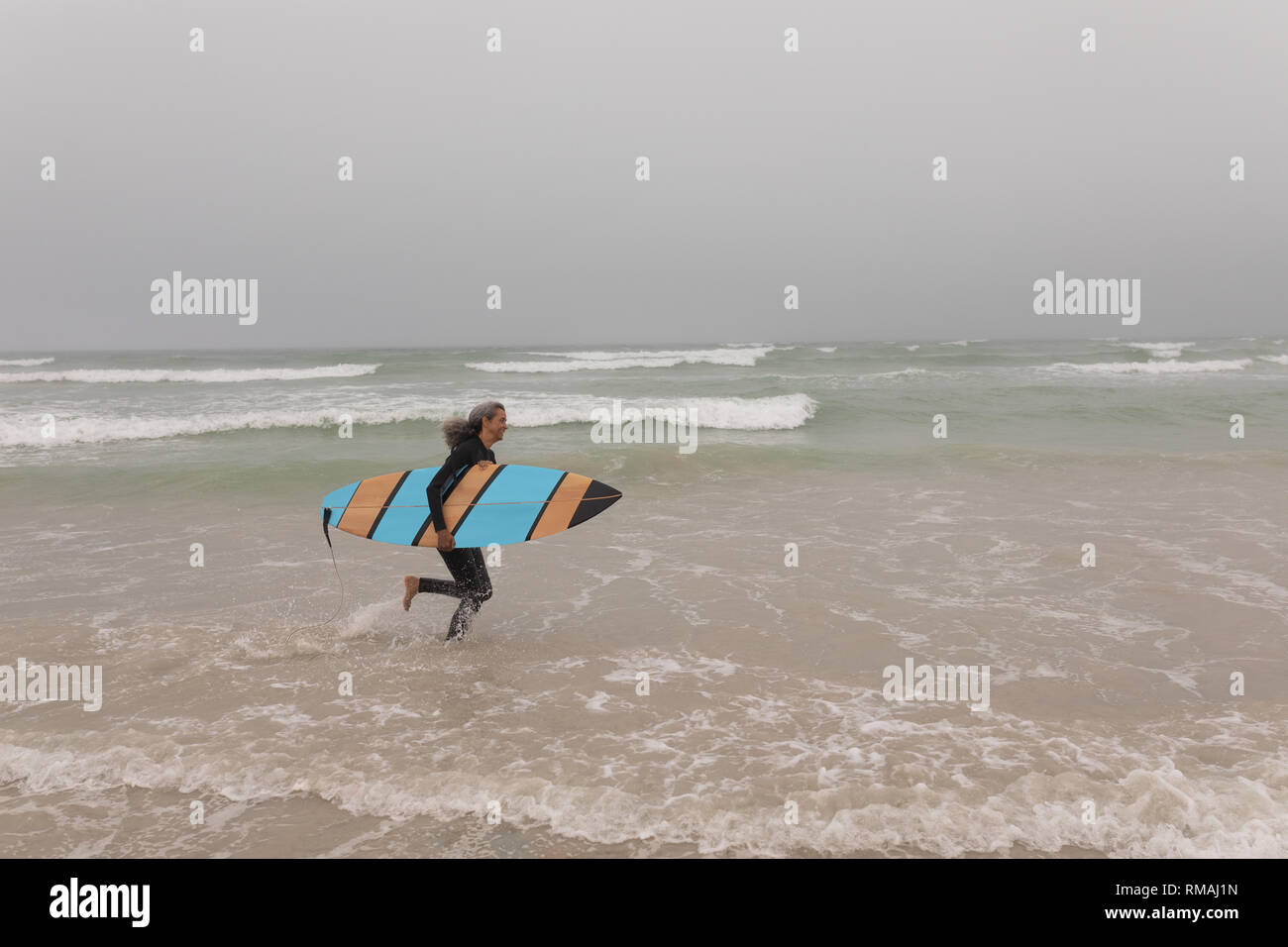 Ältere weibliche Surfer mit Surfbrett laufen am Strand Stockfoto