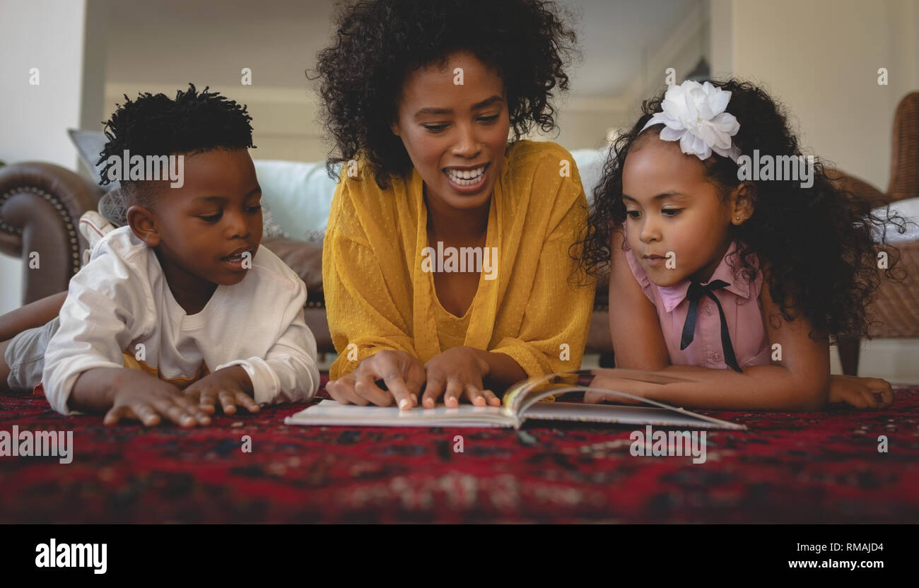 Afrikanische amerikanische Mutter mit ihren niedlichen Kinder liegen auf dem Boden und Lesen ein storybook Stockfoto