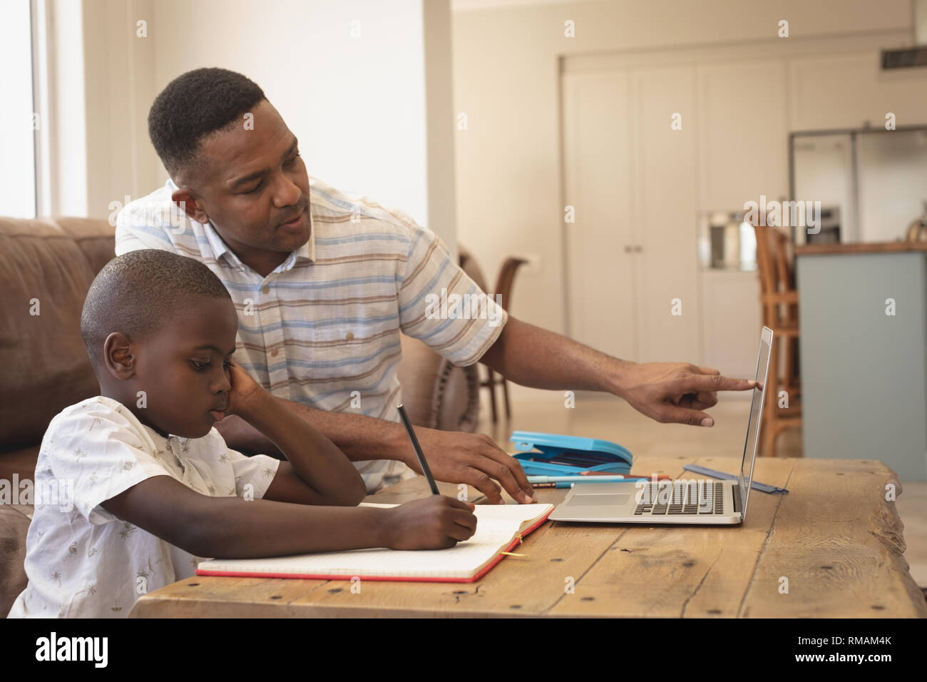 African American Vater seinen Sohn helfen bei Hausaufgaben auf Laptop am Tisch Stockfoto