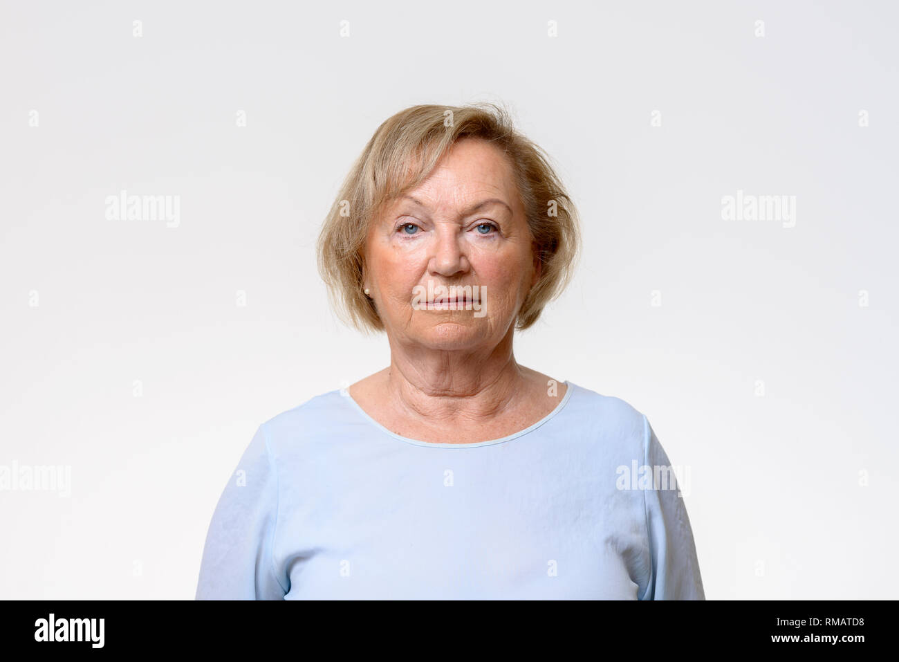 Ältere Frau direkt in die Kamera schaut mit einem intensiven spekulative Ausdruck in einem Kopf und Schultern Blick auf Weiß Stockfoto