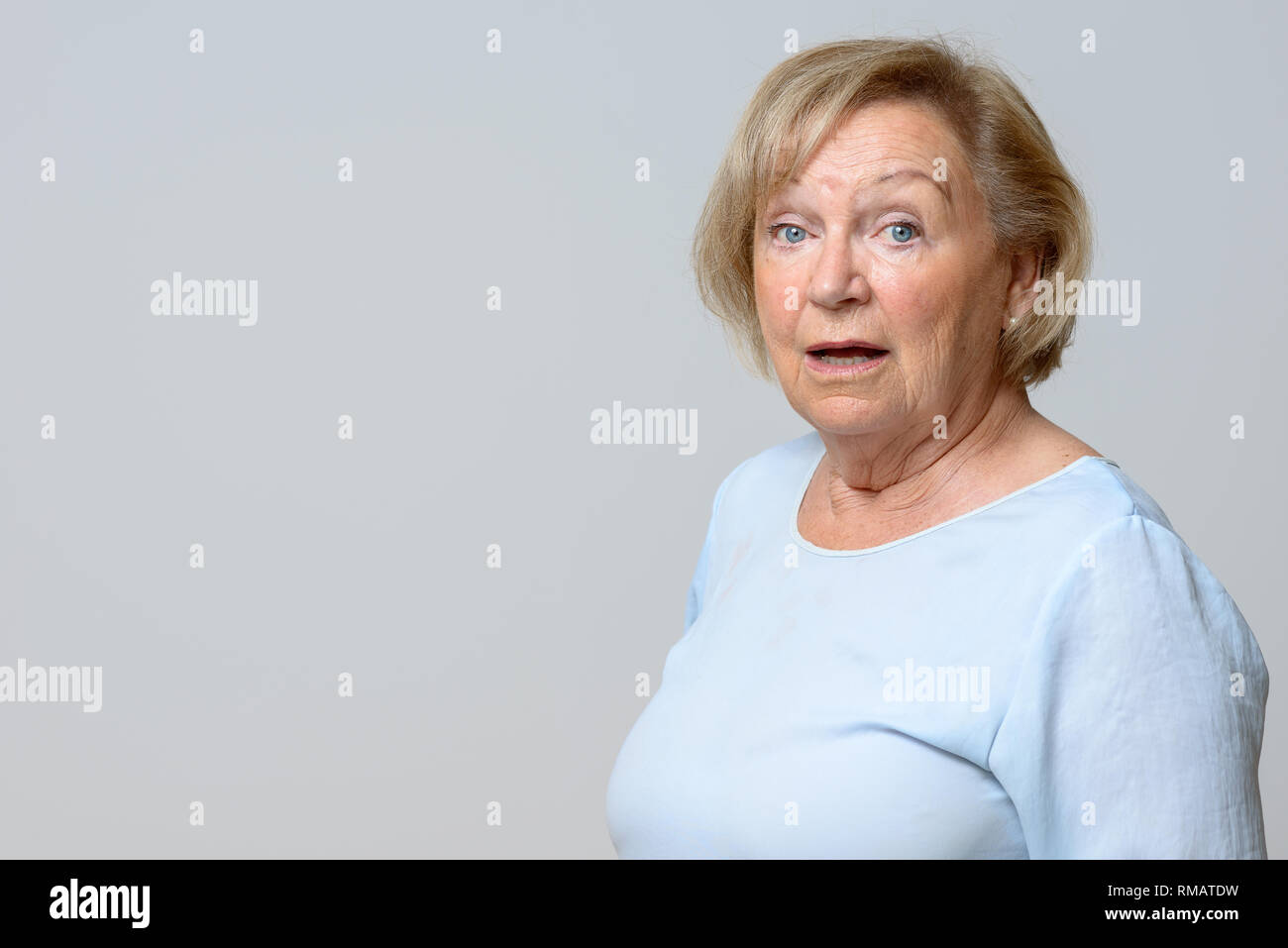 Erstaunt ältere Frau an der Kamera mit großen Augen und offenem Mund und einem überraschten natürlicher Ausdruck über Grau mit Kopie Raum suchen Stockfoto