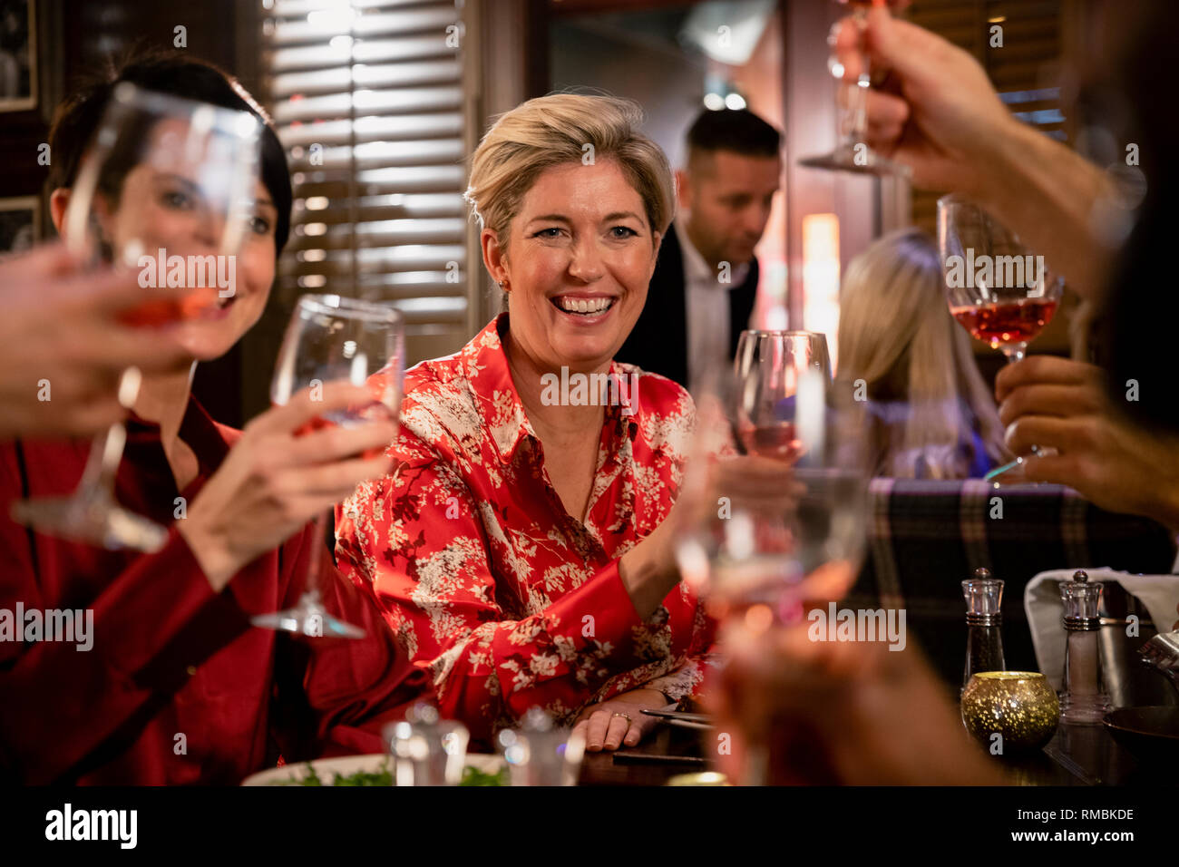 Heiter, reife Frau ihr Glas für eine feierliche Toast mit ihren Freunden in einem Restaurant ein Essen sitzen. Stockfoto