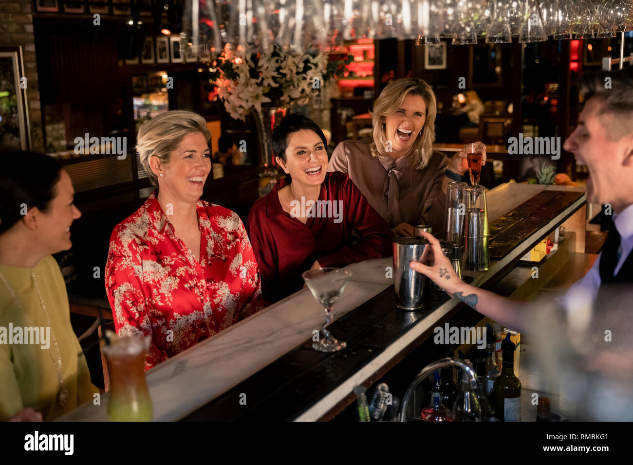 Kleine Gruppe von reifen Frauen genießen eine Nacht, sitzen an der Bar. Sie werden lachen mit den jungen Barkeeper, der ein Cocktail. Stockfoto