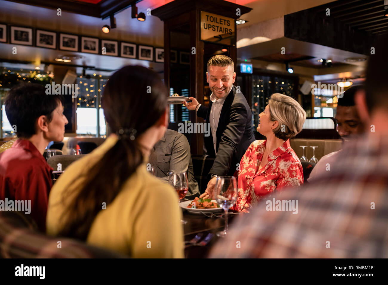 Männliche kellner Inverkehrbringen Lebensmittel nach unten auf einen Tisch, wo eine kleine Gruppe von Freunden zusammen sitzen. Stockfoto