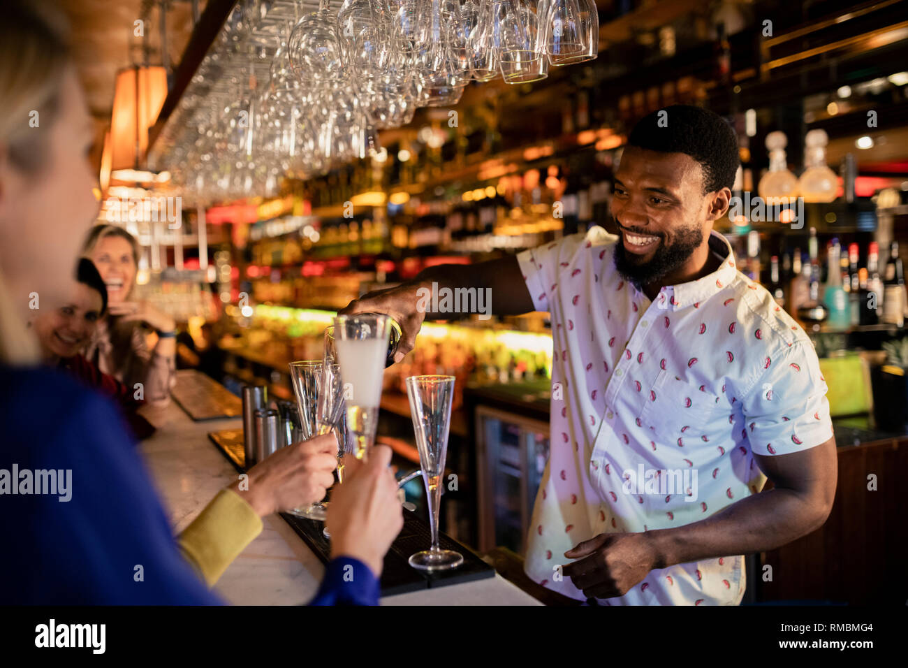 Barkeeper Befüllen eines ausgereiften womans Glas mit Prosecco. Sie sitzt an der Theke mit ihren Freunden. Stockfoto