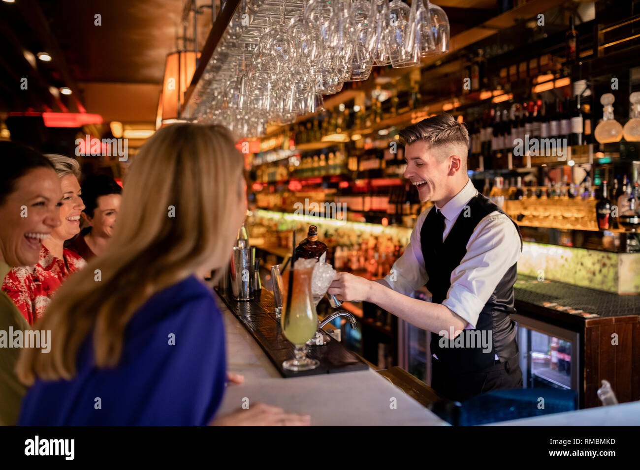 Junge Barkeeper einen Cocktail für eine kleine Gruppe von Frauen genießen Ladies Night. Sie sind alle Lachen und das Gespräch. Stockfoto