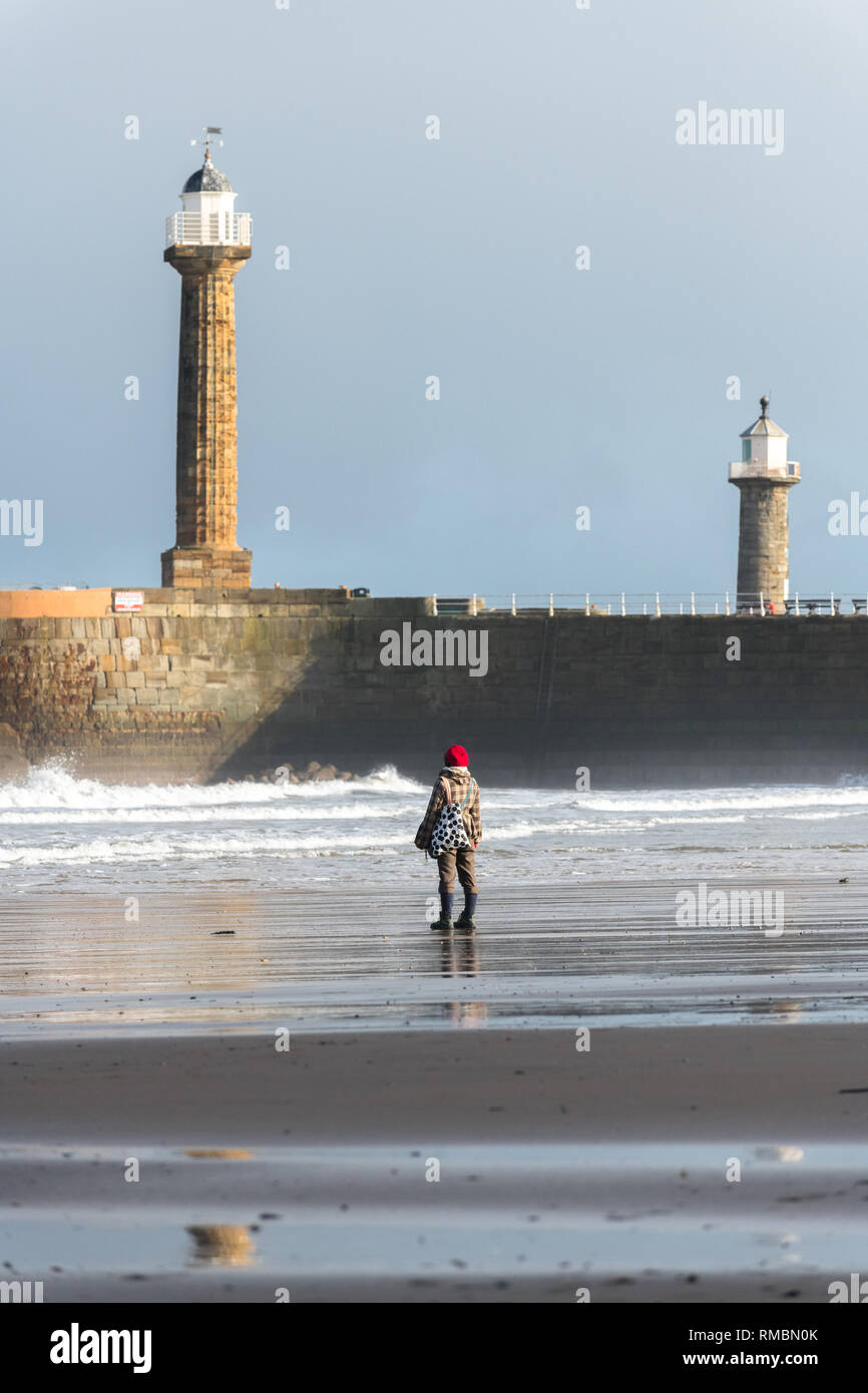 Frau am Strand von Whitby an der Küste von North Yorkshire mit den alten Leuchttürme in den Hintergrund. Stockfoto