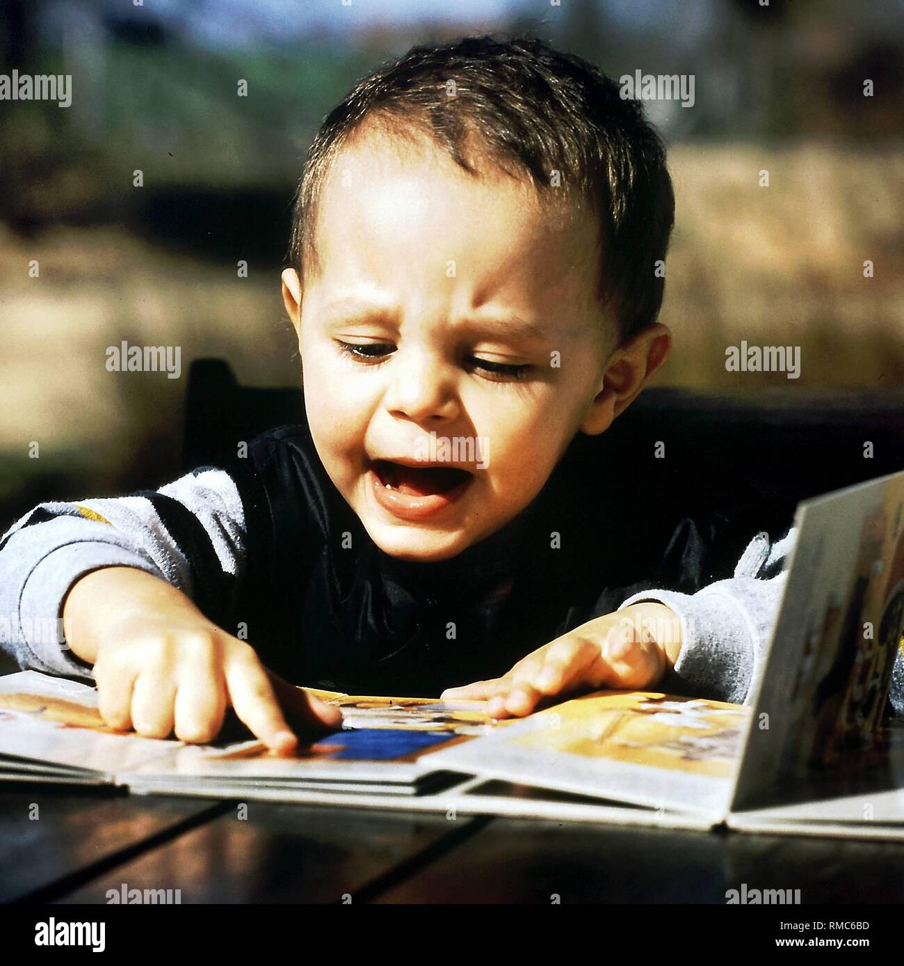 Ein kleiner Junge schaut auf ein Bilderbuch im Freien. Stockfoto