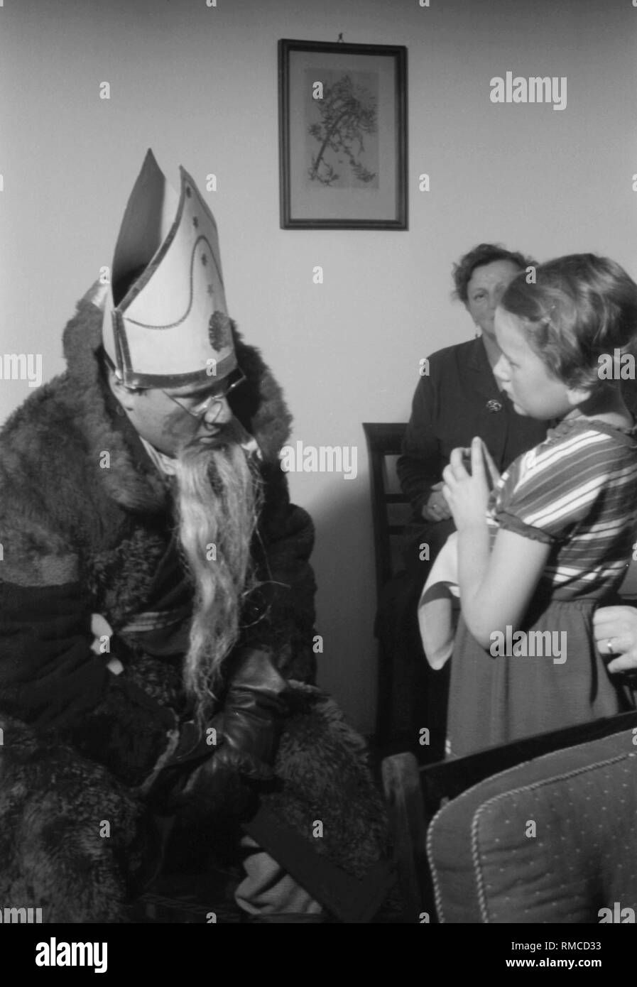 St. Nicholas spricht mit einem Mädchen in einer Münchner Klinik, vermutlich der Unifrauen-klinik in der Maistrasse (Frauenklinik Maistrasse). Im Hintergrund, die Mutter. Stockfoto
