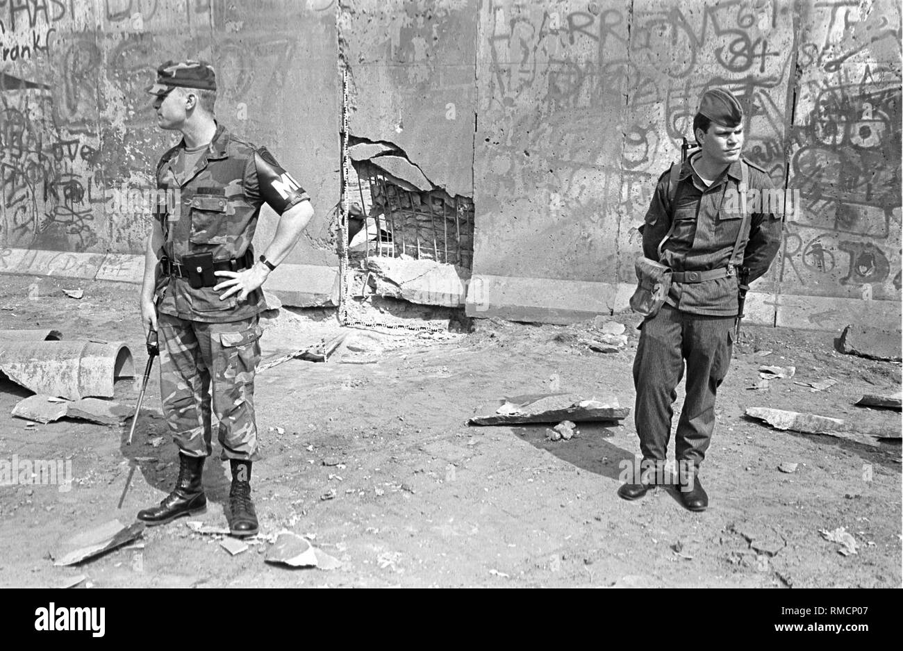 Bombenanschlag in der Berliner Mauer in der zimmerstraße an der Ecke Charlottenstraße im Stadtteil Kreuzberg in der Nähe der alliierten Grenzübergang Checkpoint Charlie. Das Bild zeigt eine US-Militär Polizist auf der linken Seite und eine DDR-Grenzsoldaten auf der rechten Seite. Stockfoto
