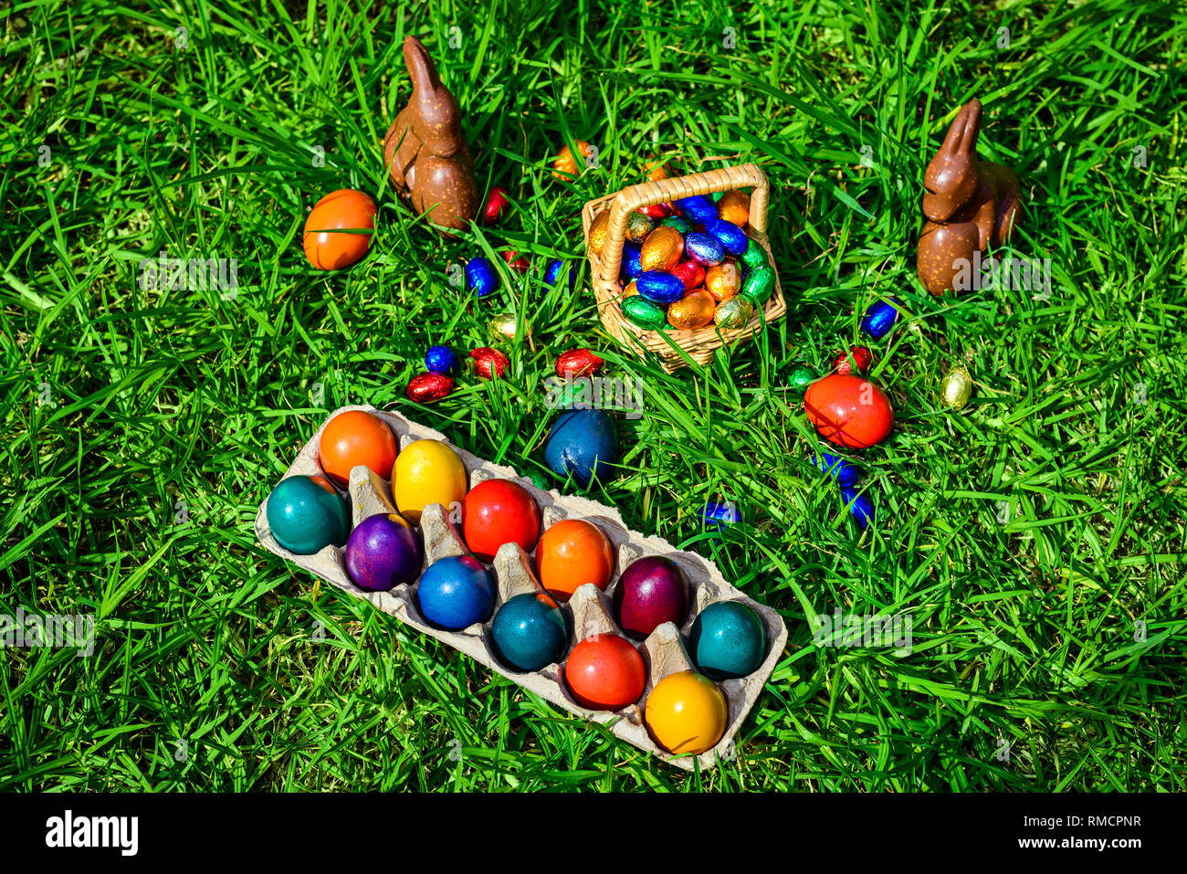 Schokolade Osterhasen, Stroh Korb voll bunter Eier auf grünem Gras Stockfoto