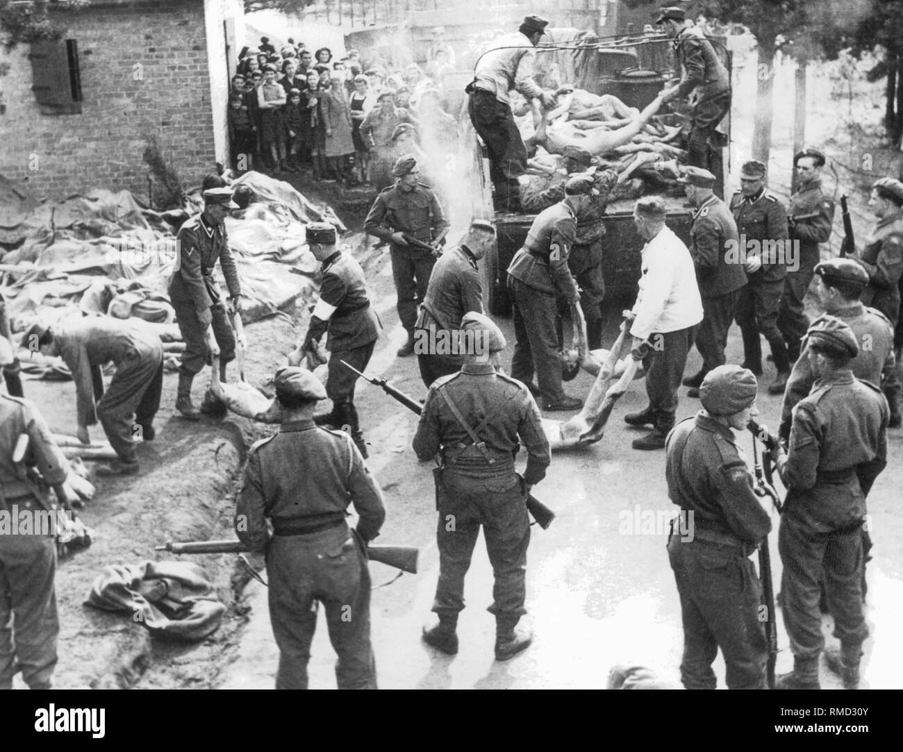 Unter der Leitung von British Guards, Mitglieder der SS-Wachmannschaften der Konzentrationslager Bergen-Belsen tragen die Leichen der Ermordeten Gefangenen zu den Massengräbern. Überlebenden Kinder im Hintergrund. Stockfoto