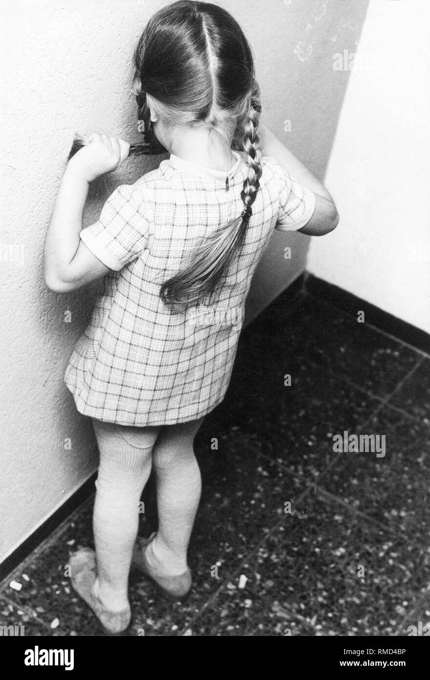 Ein kleines Mädchen hat in der Ecke des Klassenzimmers zu stehen als Strafe (inszenierte Szene). Stockfoto