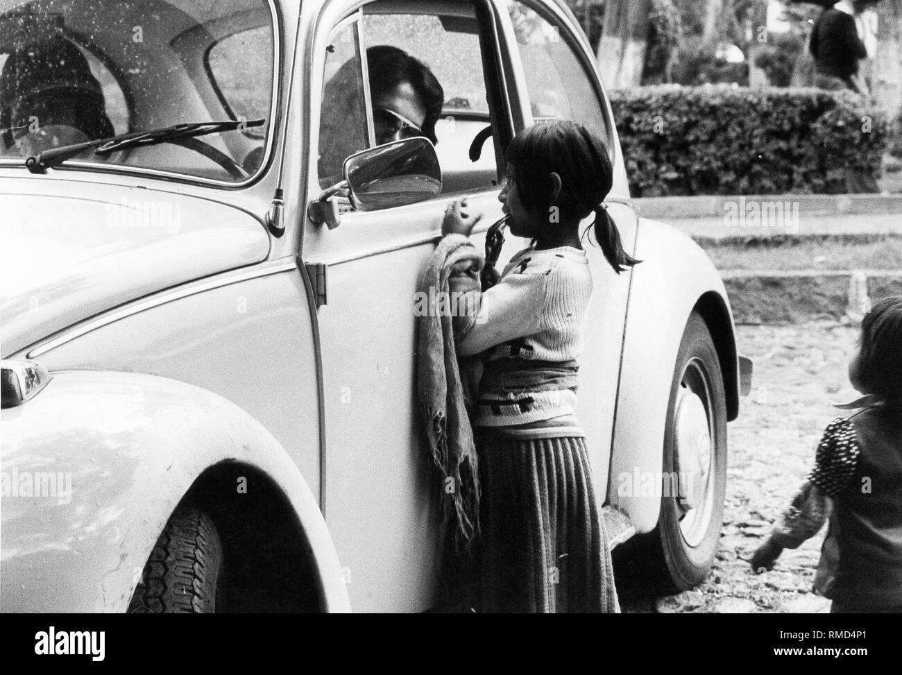 Ein kleines Mädchen bittet ein Mann in einem VW-Käfer in Mexiko Stadt. Stockfoto