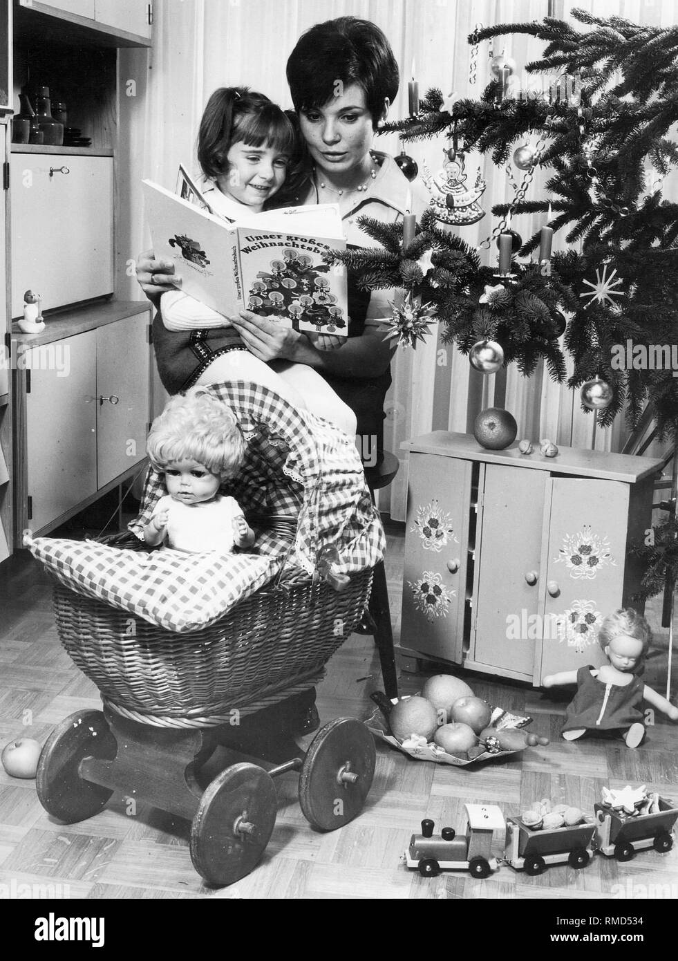 Eine Mutter liest mit ihrer kleinen Tochter unter den Weihnachtsbaum nach der Übergabe der Geschenke. Stockfoto