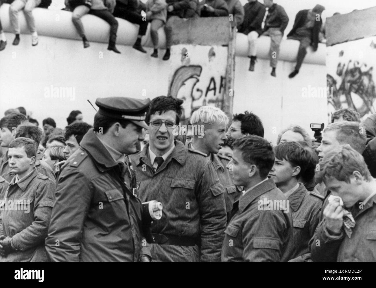 Nach dem Fall der Berliner Mauer, Polizisten von West Berlin und Grenztruppen der DDR zusammen kommen. Im Hintergrund, Berliner sitzen auf der Mauer. Stockfoto