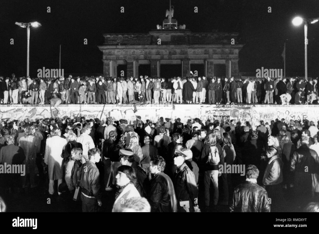 Kurz nachdem die Mauer geöffnet wurde, eine Masse von Menschen steht an der Wand, vor dem Brandenburger Tor und der Berliner Mauer. Es ist Nacht. Stockfoto