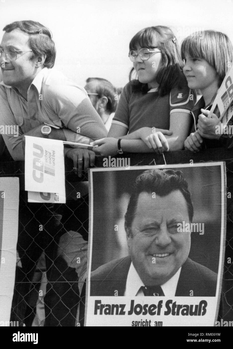 Dieses Foto zeigt eine Familie, mit verschiedenen Wahlen Werbemittel Zubehör ausgestattet, in der das Publikum auf einer Wahlkampfveranstaltung der Union. Auf dem Zaun hängt ein Plakat gibt bekannt, dass das Erscheinungsbild der Kanzlerkandidat der Union, CSU, Franz Josef Strauß. Stockfoto