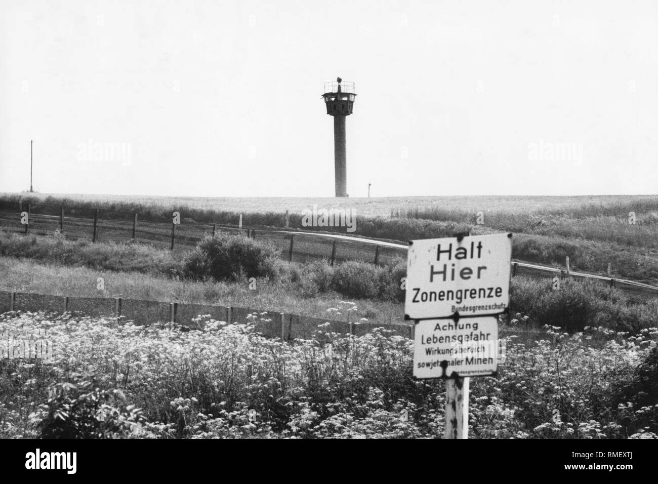 Blick auf die Grenze zwischen Deutschland und der DDR mit Aussichtsturm und Warnschilder vor Minen, Undatiertes Foto (um 1980). Stockfoto