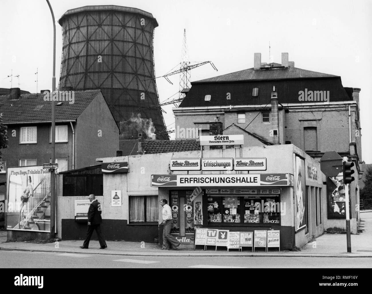 Blick auf einen Kiosk in einer Reihe von Häusern an der Kaertener Ring in Gelsenkirchen. Vor dem Kiosk gibt es Zeichen Werbung Zeitungen und Zeitschriften. Im Hintergrund eine hohe Spannung Pylon und einer hölzernen Kühlturm. Undatiertes Foto. Auf der Kiosk ist ein Zeichen der Stern-Brauerei aus Essen. Diese geschlossen in 1989. Stockfoto