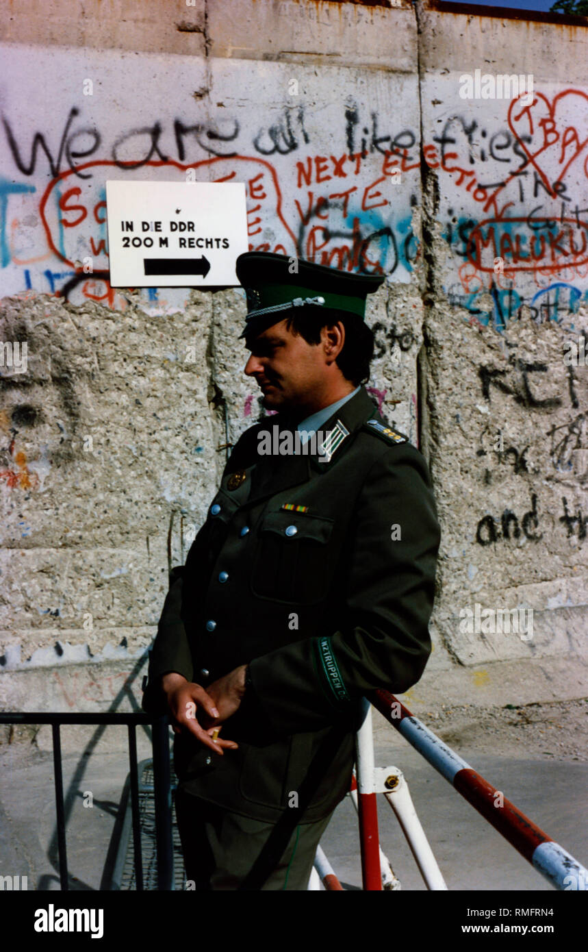 Ein DDR-Grenzsoldaten lehnt sich gegen Hindernisse vor der Mauer am Brandenburger Tor. Stockfoto