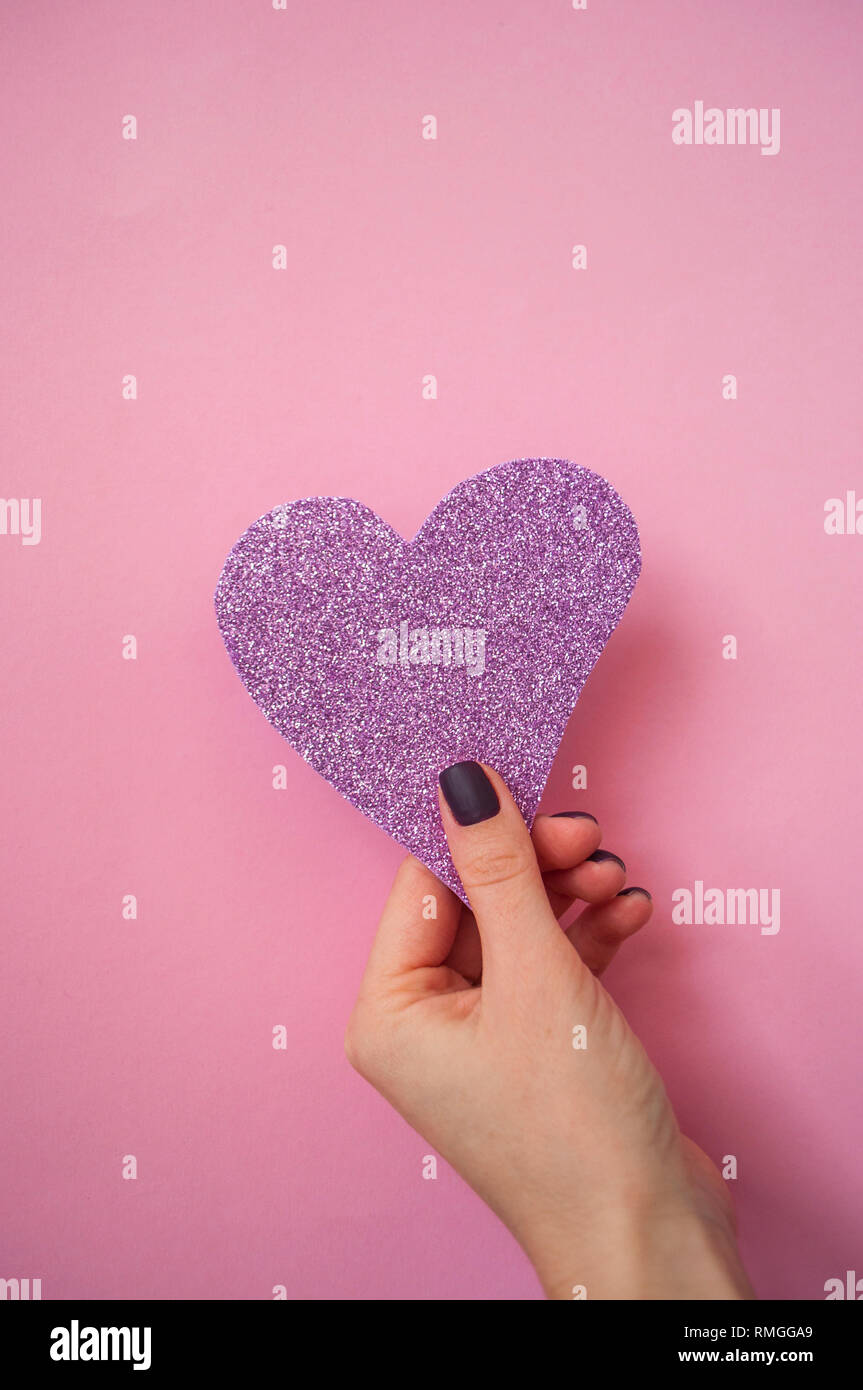 Die junge Frau mit schönen Maniküre auf Pastell rosa Hintergrund holding Rosa glitzerndes Herz. Stockfoto